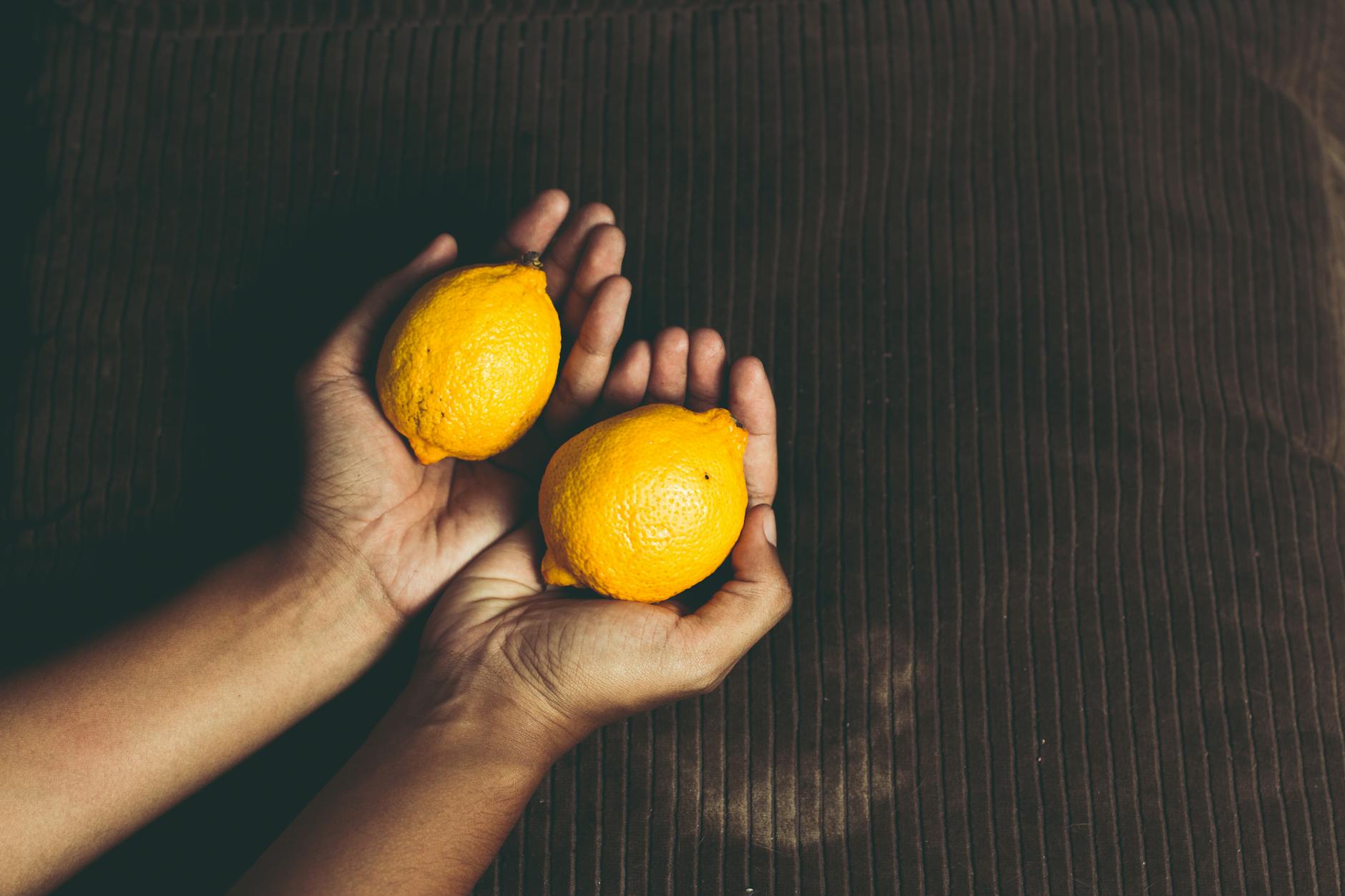 Dos limones frescos en manos abiertas sobre fondo marrón, simbolizando sensibilidad y adaptación
