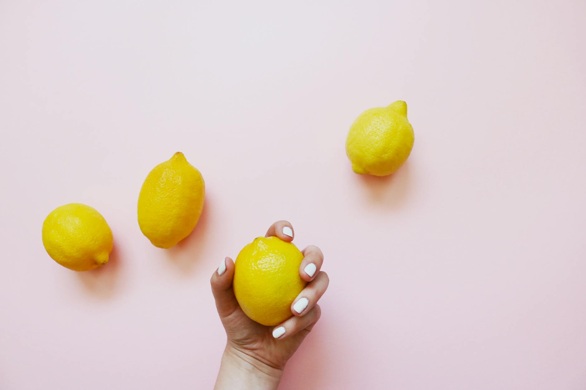 A hand holding a lemon on soft pink background, symbolizing natural pleasure and citrus-inspired intimate wellness