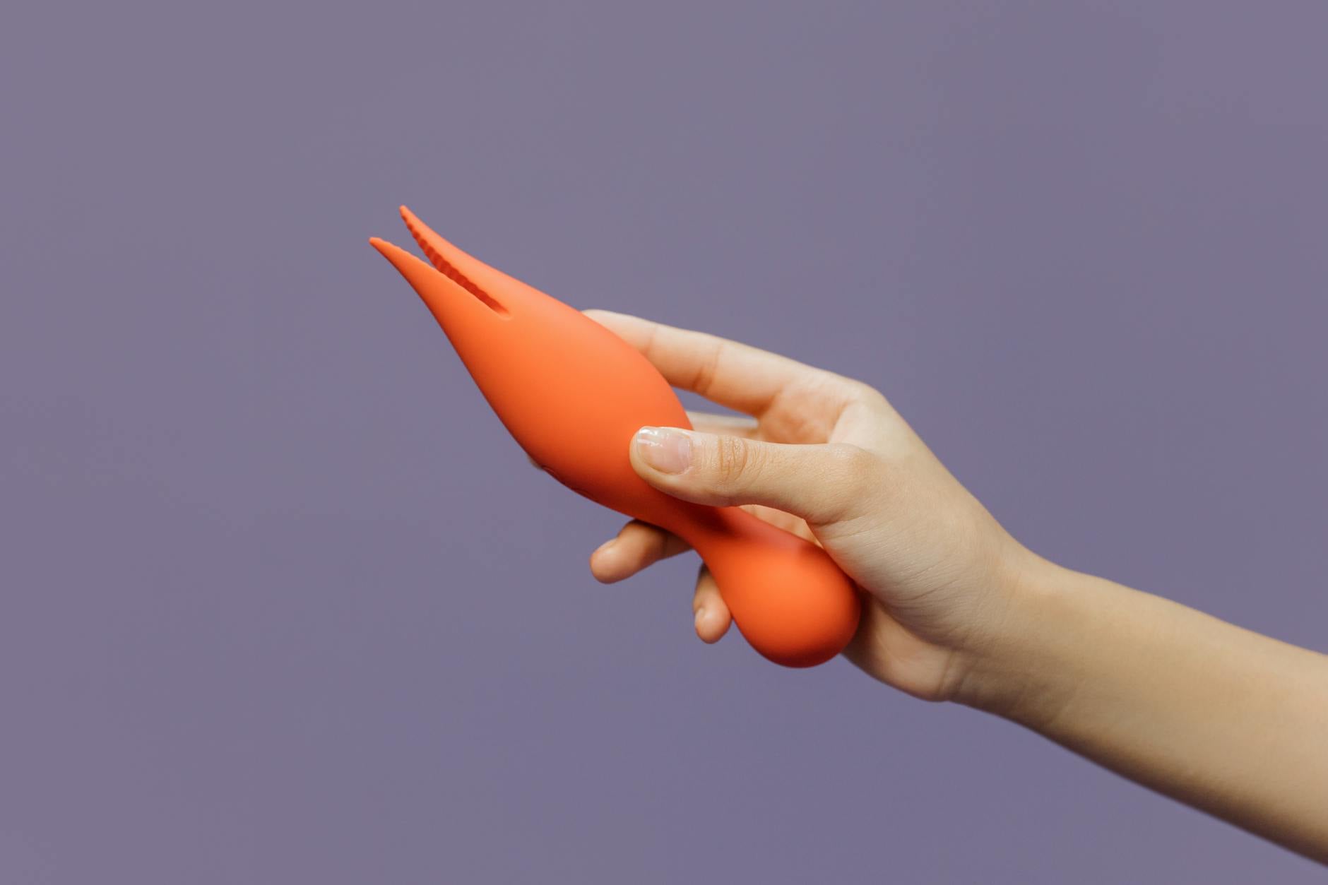 A hand reaching over a variety of colorful sex toys arranged on a table