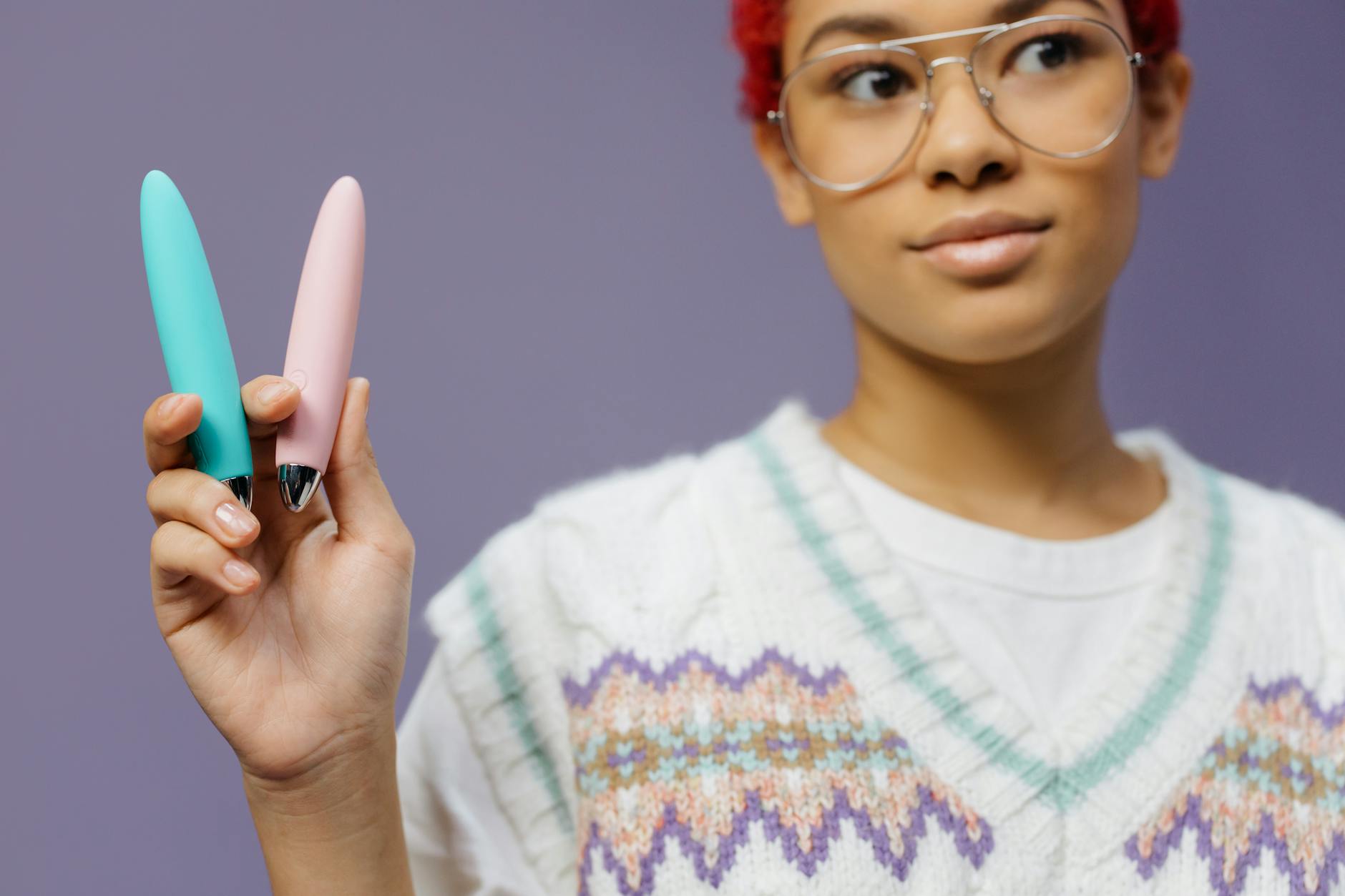 Woman holding colorful vibrators against a purple background, expression showing contemplation and self-awareness.