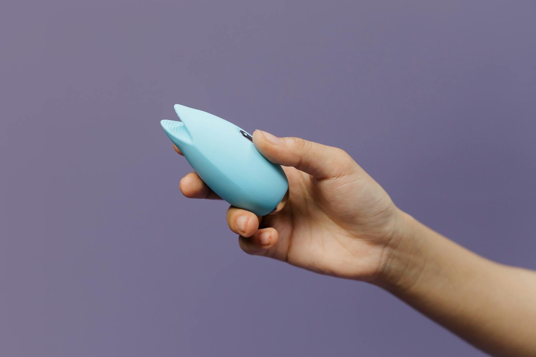 Hand reaching over a variety of colorful sex toys, showing multiple options