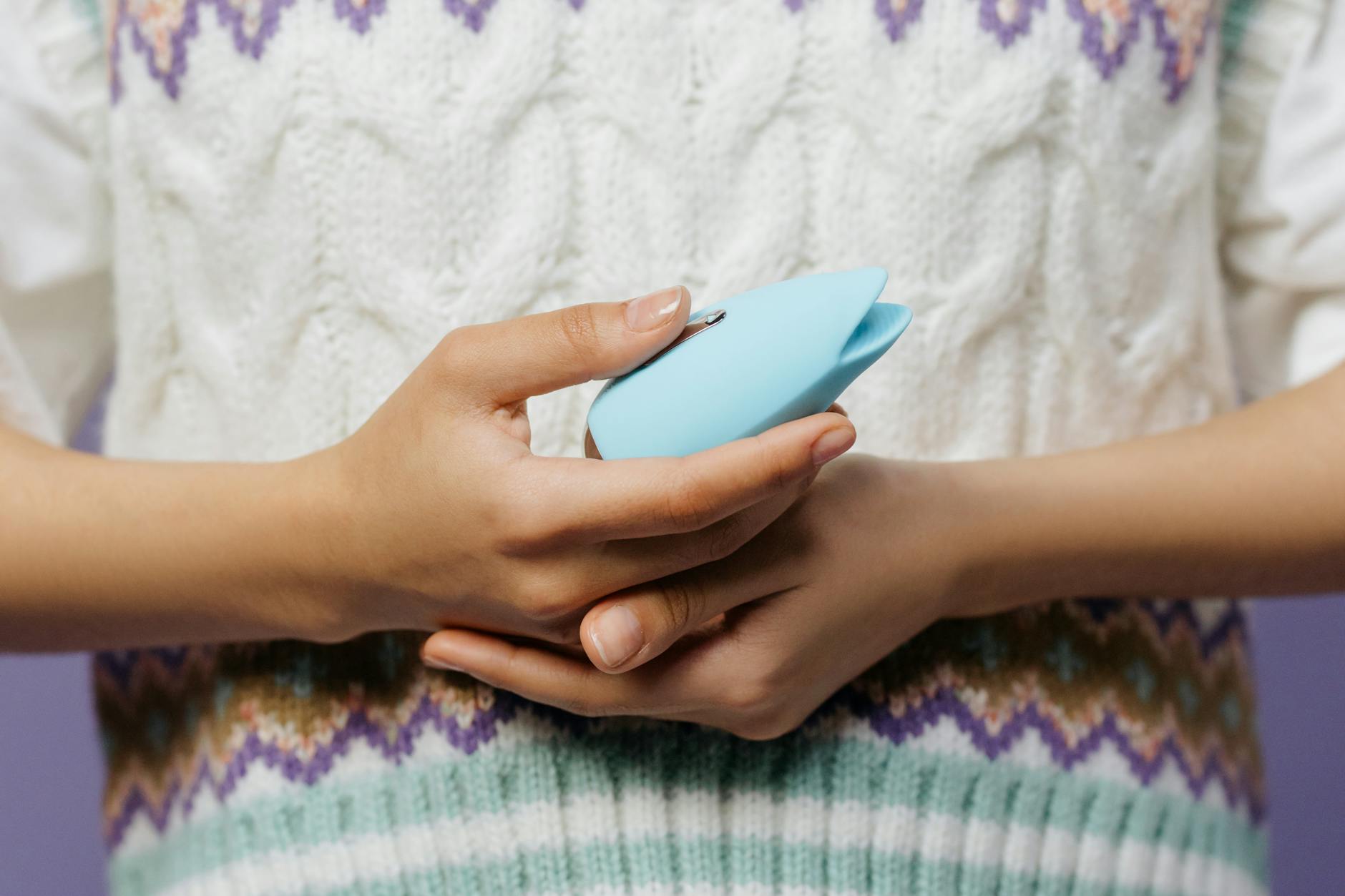 A blue silicone clitoral vibrator held in hand against a solid purple background, symbolizing self-directed pleasure and autonomy.