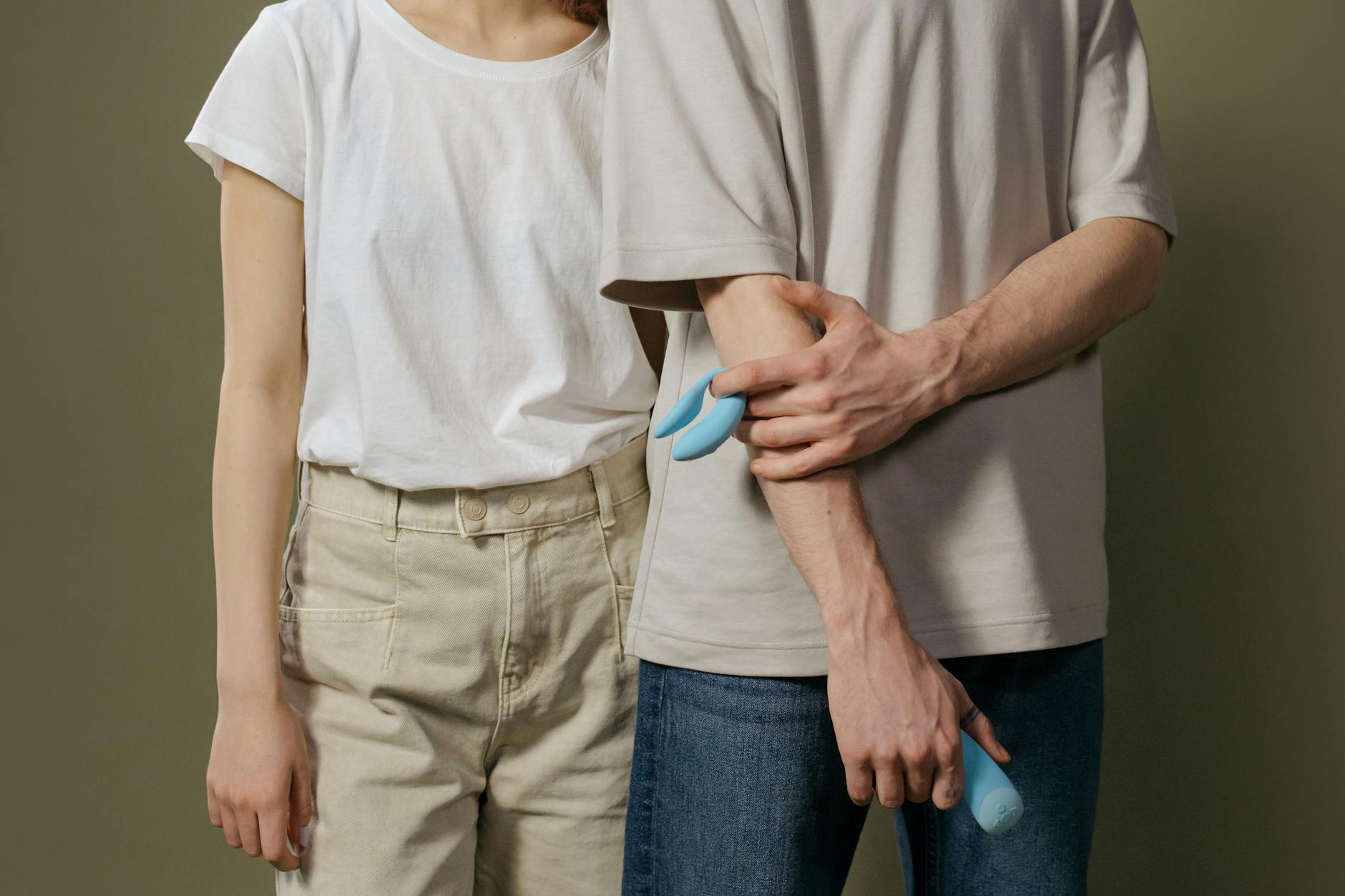 A hand holding a blue silicone sex toy against a purple background