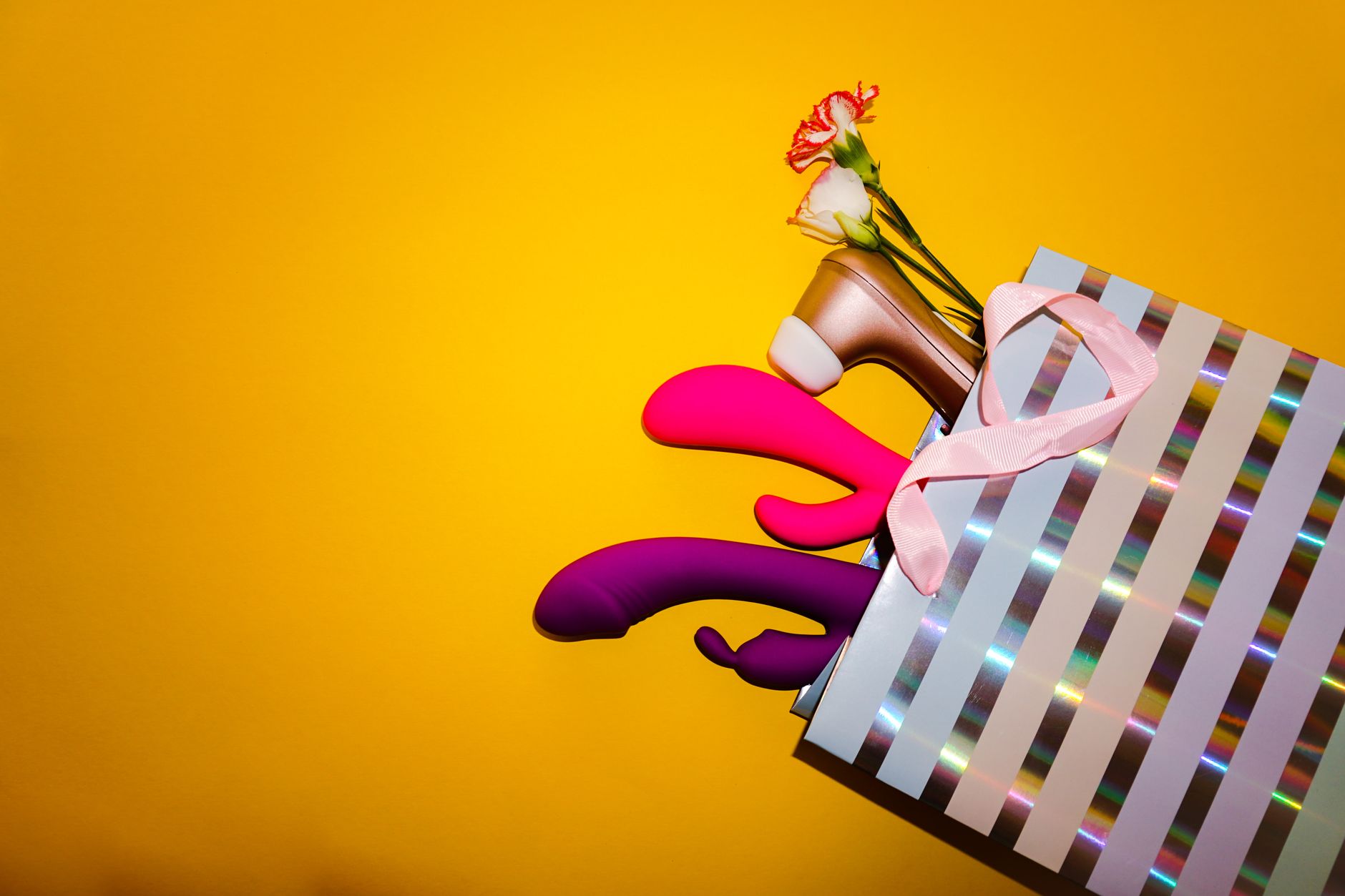 Vibrant arrangement of various colorful sex toys on a bright yellow surface, showcasing diversity of design and function